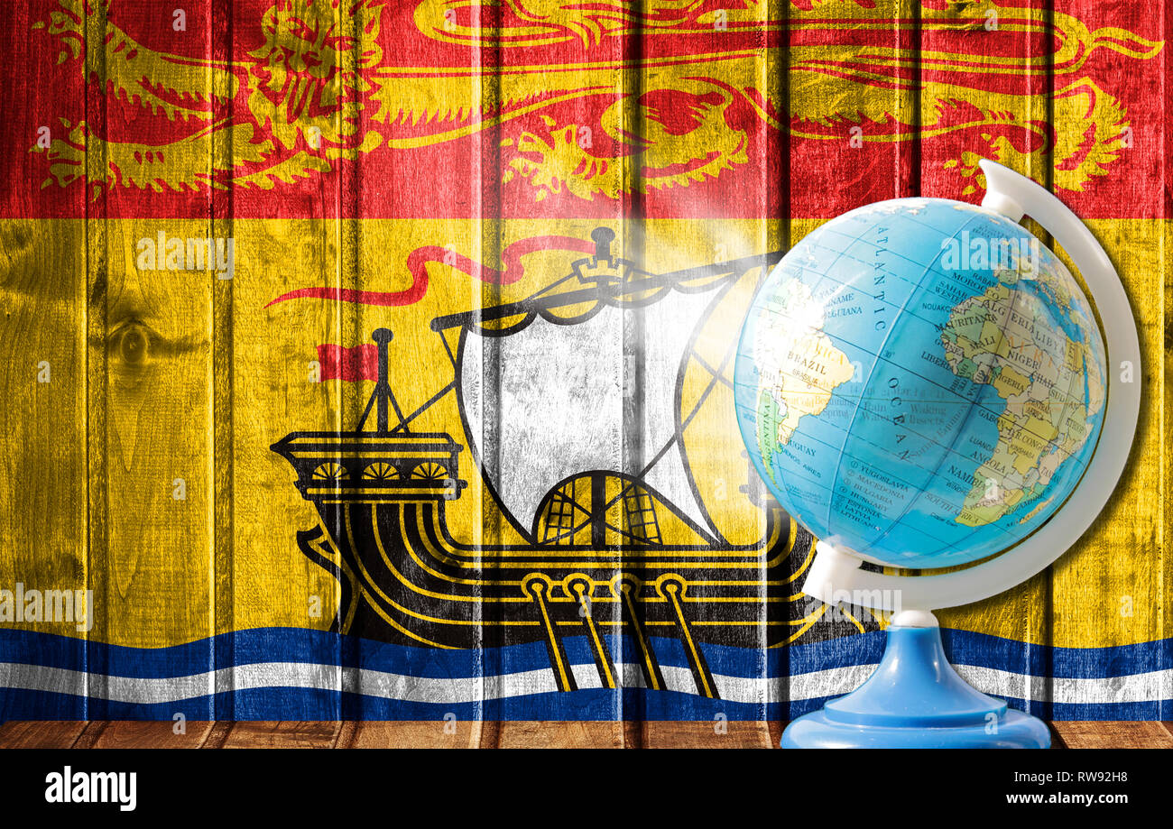 Globus mit einer Weltkarte auf einem hölzernen Hintergrund mit dem Bild der Flagge von New Brunswick. Das Konzept der Reisen und Freizeit im Ausland. Stockfoto