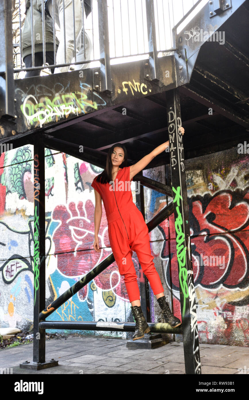 Eine schöne asiatische Mädchen in einem Sexy Red jumpsuit unterhalb und industriellen Posen, Graffiti "Treppenhaus - Sie glücklich aussieht und Spaß haben Stockfoto
