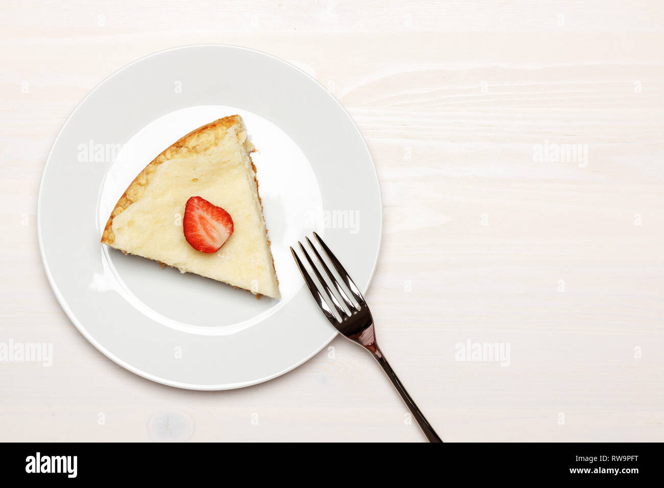 Zusammensetzung mit einem Stück Käsekuchen auf einer hölzernen weissen Tisch. Ansicht von oben Stockfoto