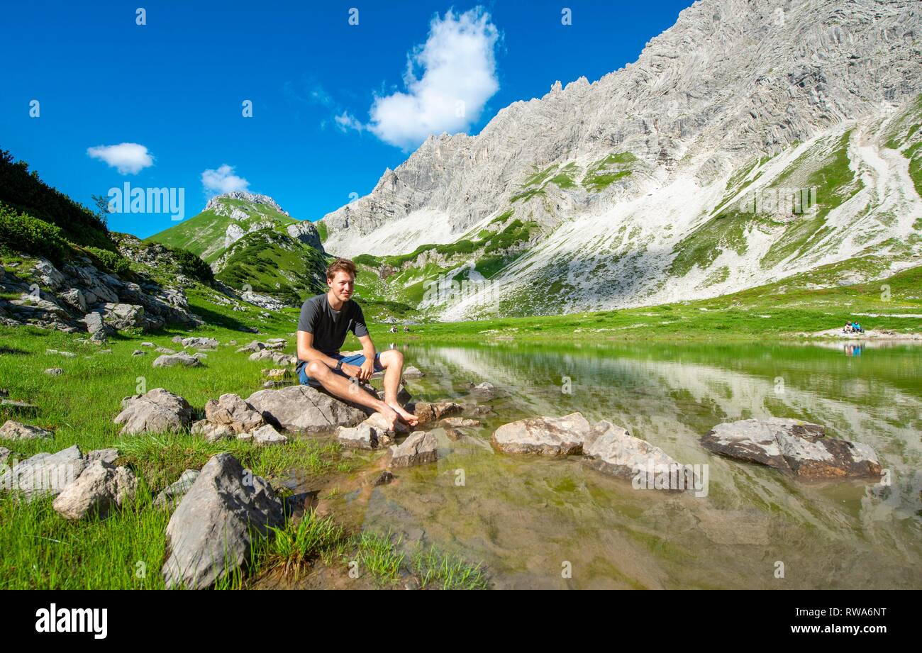 Junger Mann sitzt auf Stein, Berg See am Prinz-Luitpold-Haus, Allgäuer Alpen, Bad Hindelang, Allgäu, Bayern, Deutschland Stockfoto