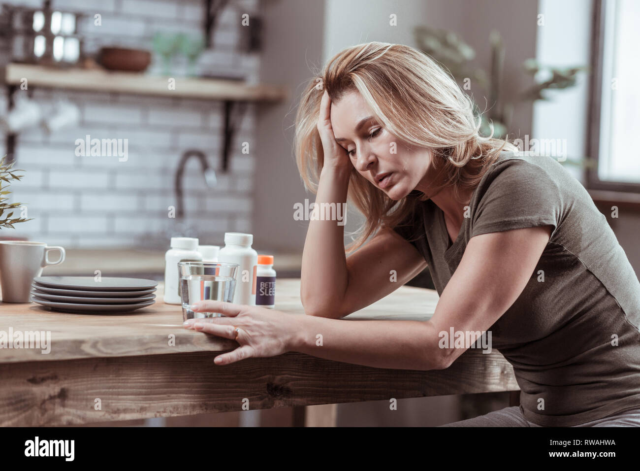 Blonde Frau in der Küche sitzt und die Einnahme von Medizin Stockfoto