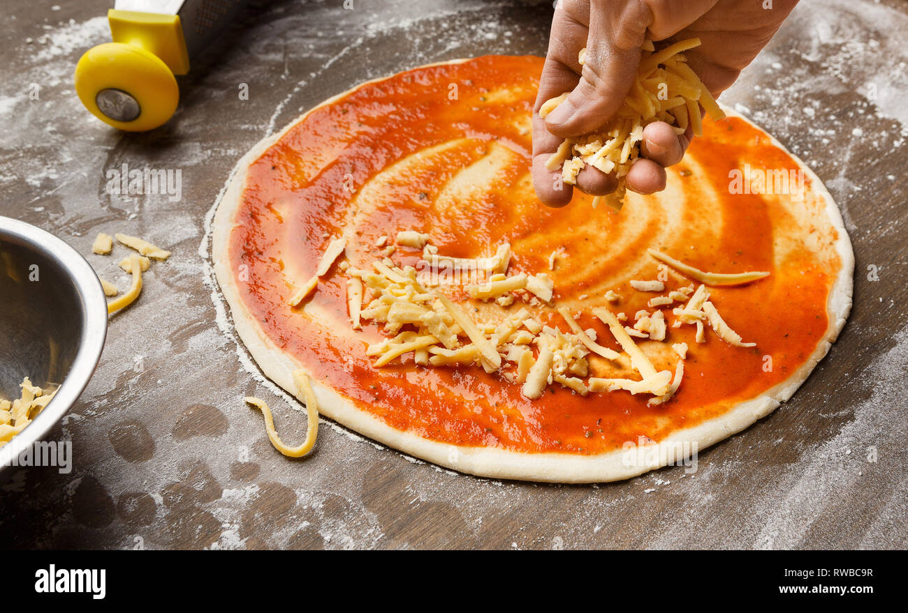 Mann hinzufügen Käse Pizza in der Küche Stockfoto