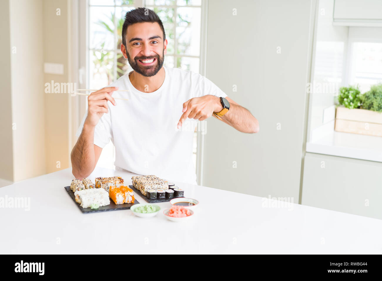 Stattliche Hispanic Mann essen asiatische Sushi mit Stäbchen sehr glücklich zeigte mit Hand und Finger Stockfoto