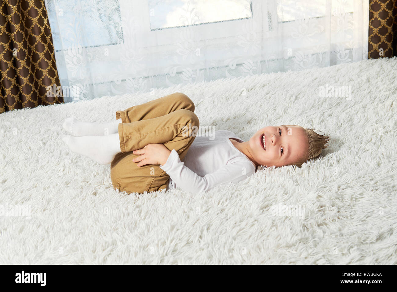Kind gesund nach Hause. Gerne kleine junge Blondine auf weiche Tagesdecke Bett lag, Ansicht von oben. Kleines Kind lacht während Kamera schaut. Stockfoto