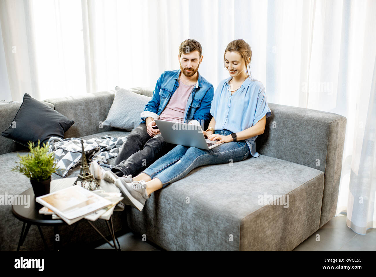 Junges Paar gekleidet lässig in blauen Shirts sitzen auf der Couch mit dem Laptop zu Hause Stockfoto
