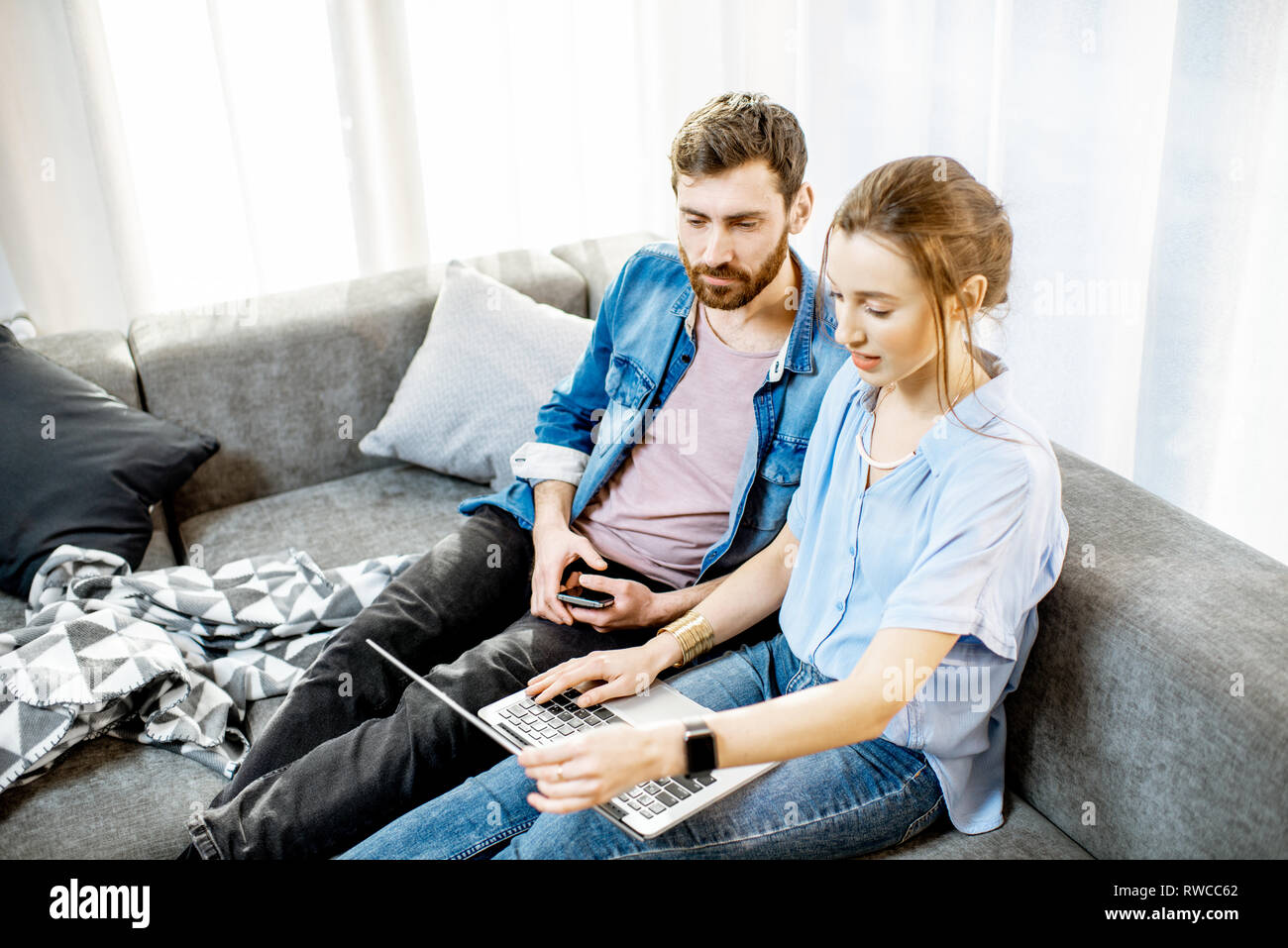 Junges Paar gekleidet lässig in blauen Shirts sitzen auf der Couch mit dem Laptop zu Hause Stockfoto