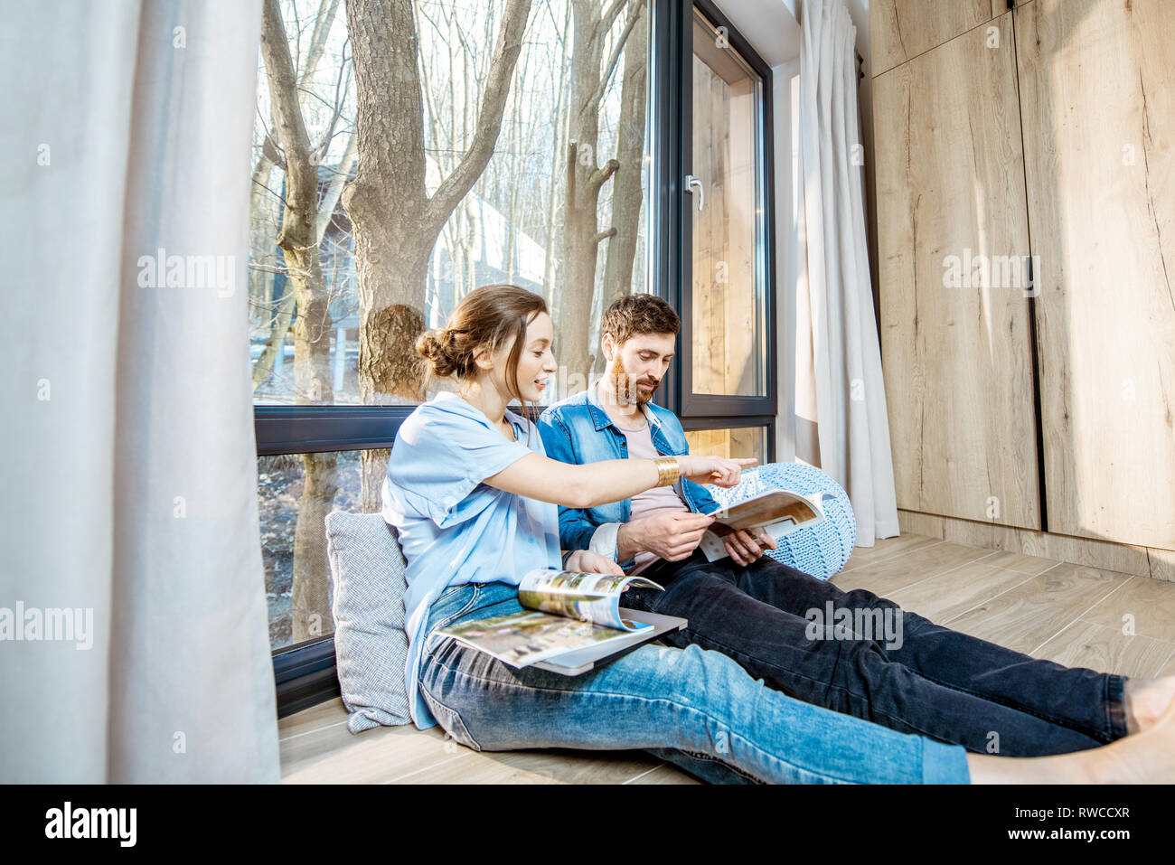 Glückliches Paar zusammen sitzen auf dem Boden in der Nähe der Fenster mit schöner Aussicht, lesen einige Zeitschriften und Entspannung zu Hause Stockfoto