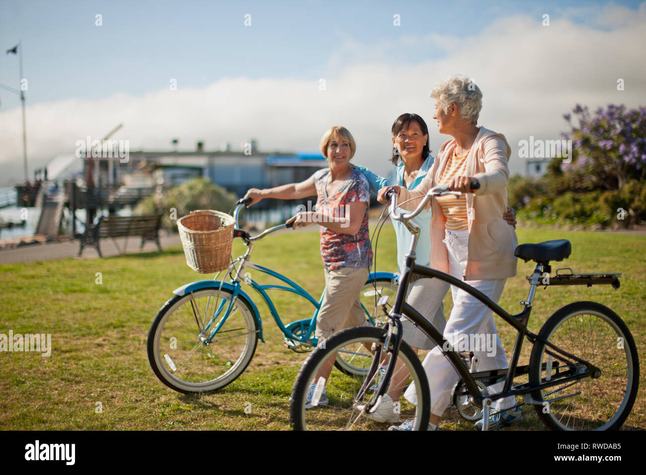 Drei reife weibliche Freunde haben Spaß miteinander chatten, während Sie Ihre Fahrräder durch einen grünen Park entfernt. Stockfoto