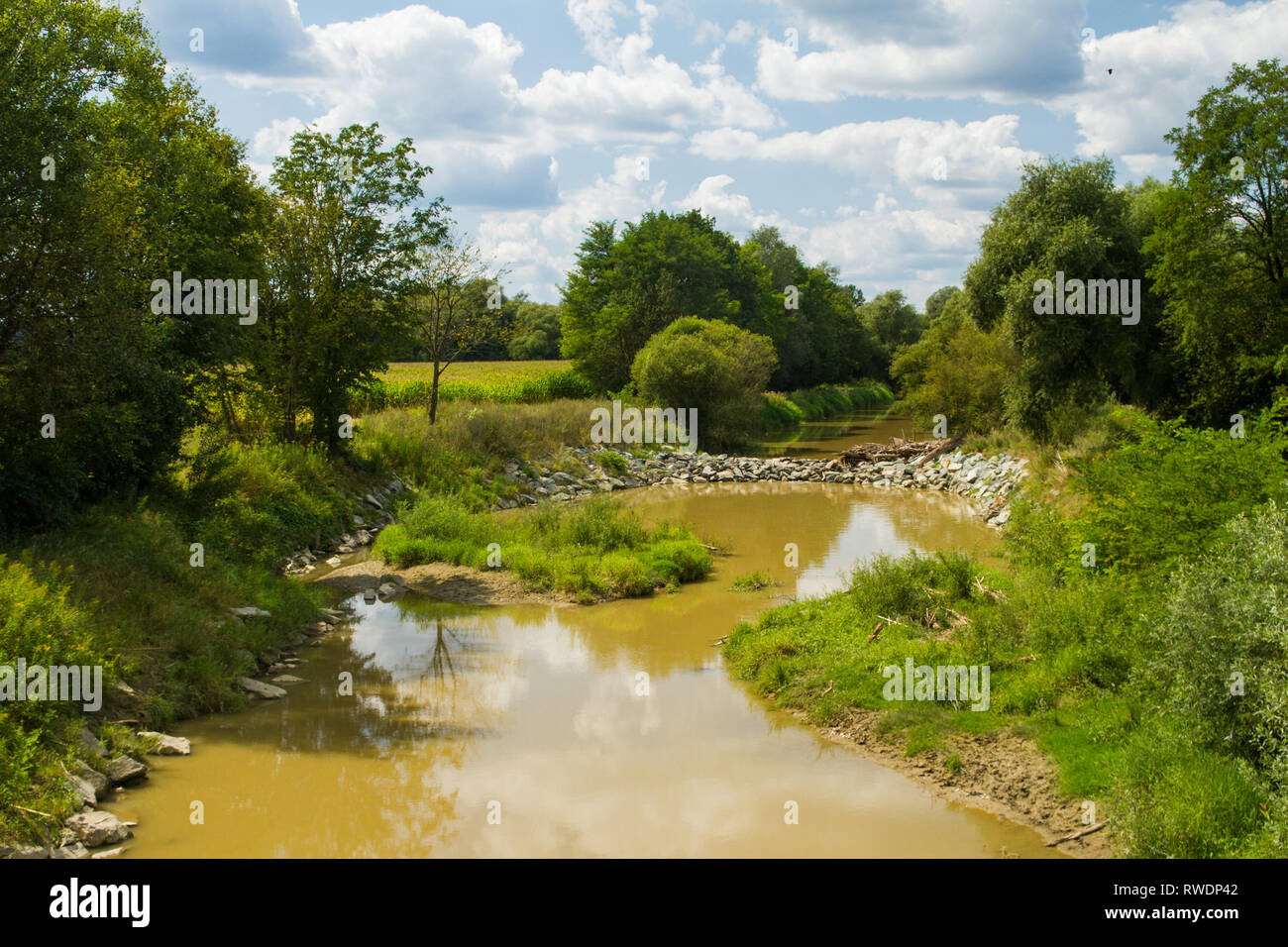 Blick auf den Raab, Fluss Raba Riverbed von Bäumen und Gebüsch auf River Bend umgeben. Sommer, blauer Himmel mit Wolken. Grenze Fluss. Braunes Wasser. Österreich Stockfoto