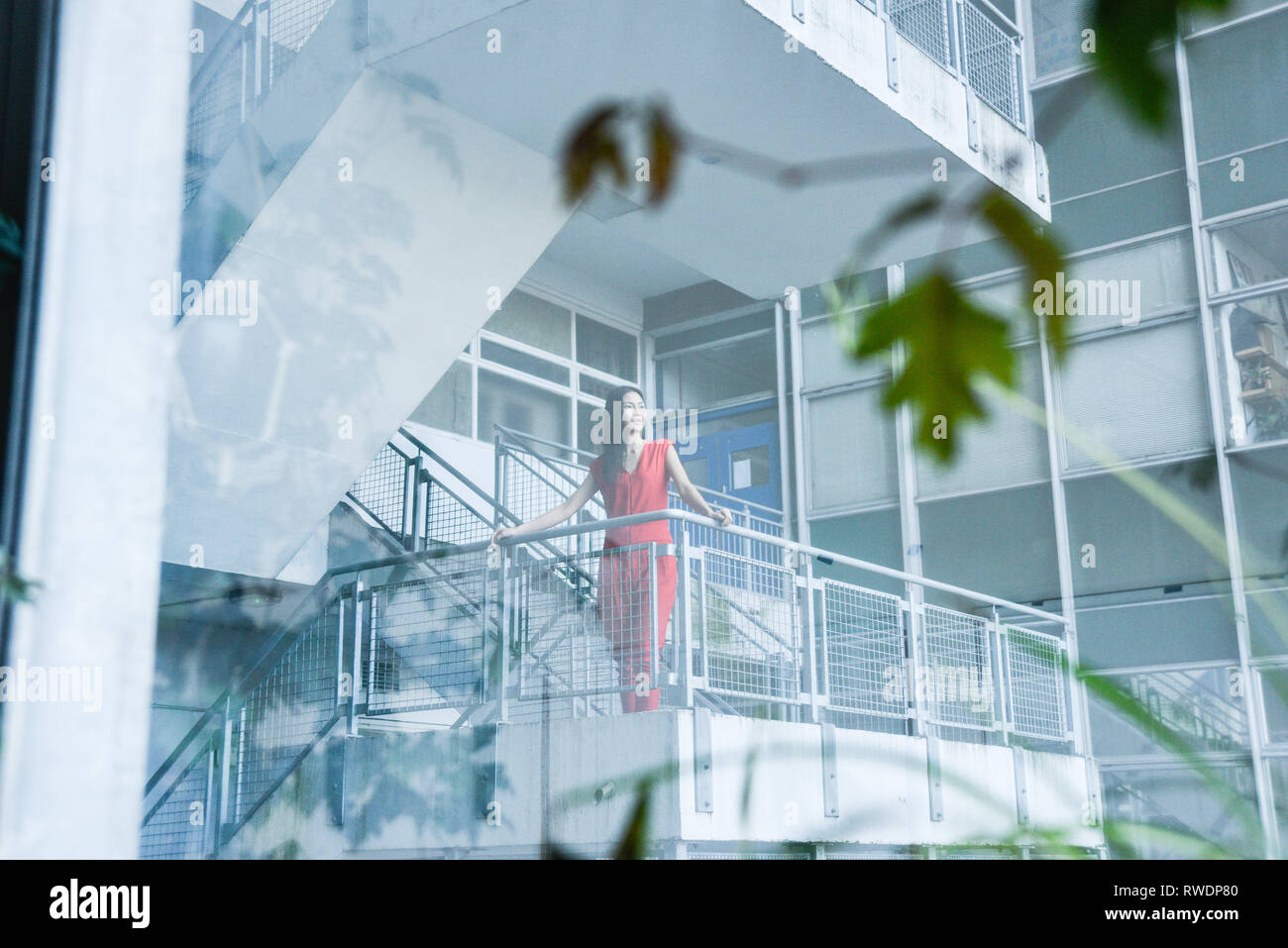 Eine schöne asiatische Mädchen in einem Sexy Red jumpsuit steht auf einem Hochhaus Treppenhaus mit Windows und Büros im Hintergrund - Sie sieht glücklich aus und städtischen Stockfoto