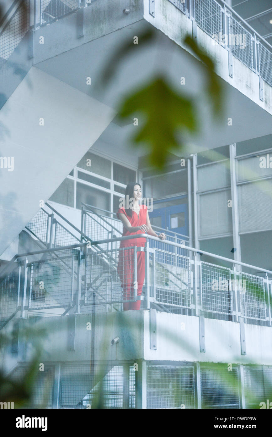 Eine schöne asiatische Mädchen in einem Sexy Red jumpsuit steht auf einem Hochhaus Treppenhaus mit Windows und Büros im Hintergrund - Sie sieht glücklich aus und städtischen Stockfoto