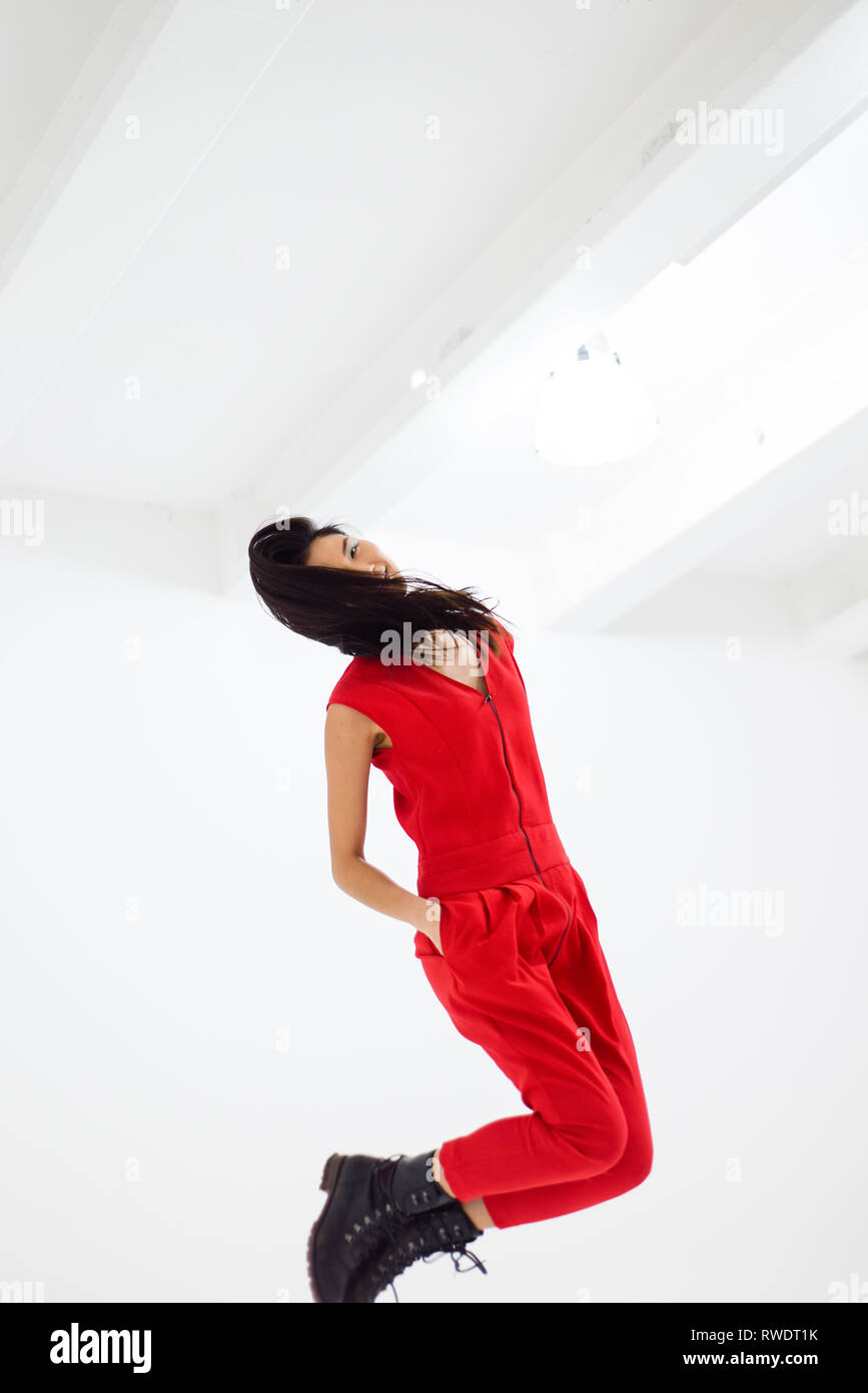 Eine schöne asiatische Mädchen stehen in einem komplett weißen Zimmer springt und schüttelt ihre langen schwarzen Haare um - sie trägt einen roten Overall Stockfoto