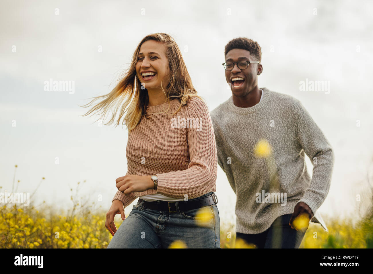 Glücklich der Mann und die Frau, die auf der Wiese Spaß haben. Paar spielen und laufen durch eine blühende Wiese im Freien. Stockfoto