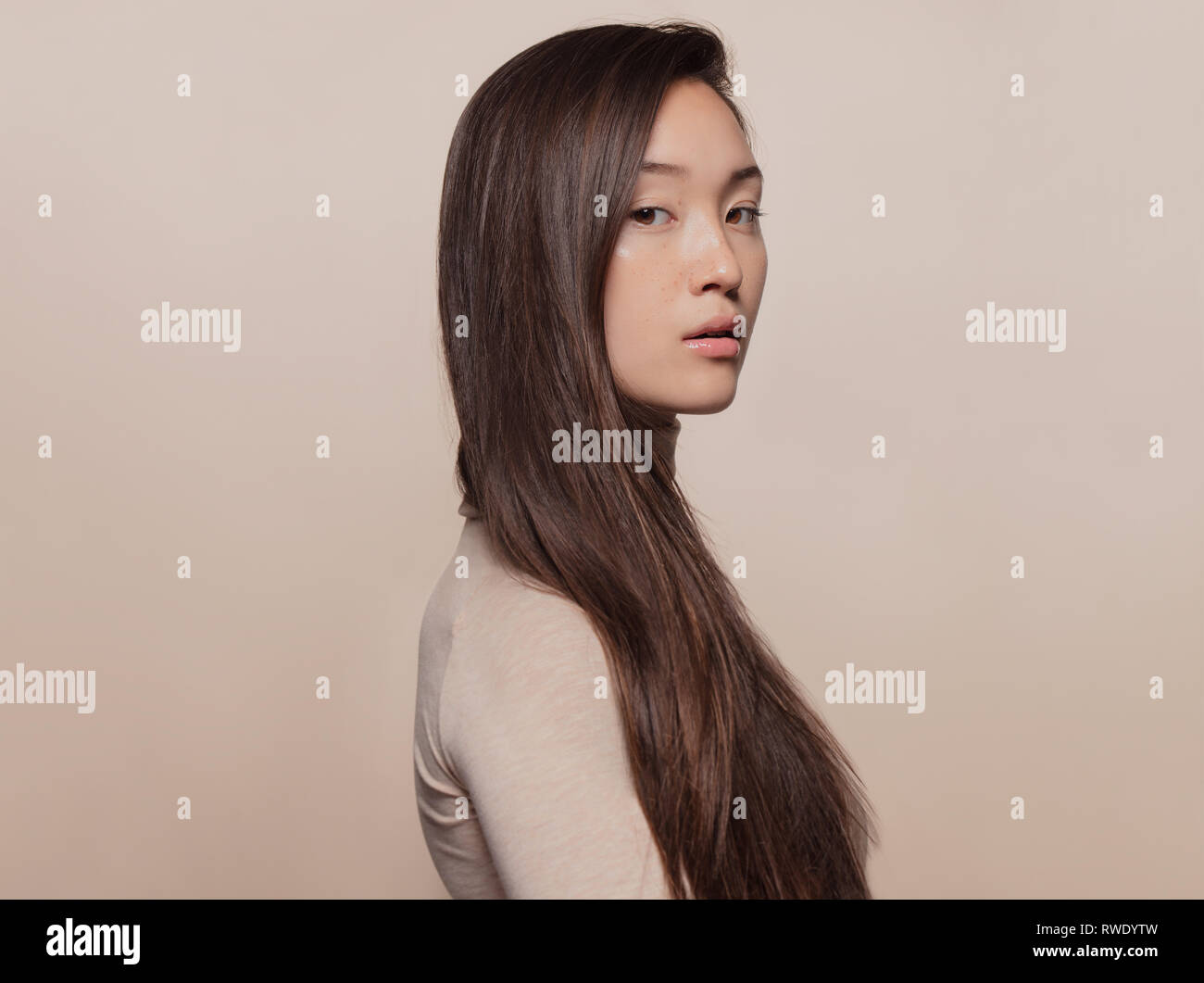 Porträt der schönen jungen Frau mit langen braunen Haaren gegen beigen Hintergrund. Asiatische Frau mit einer langen, geraden, das Haar an der Kamera. Stockfoto