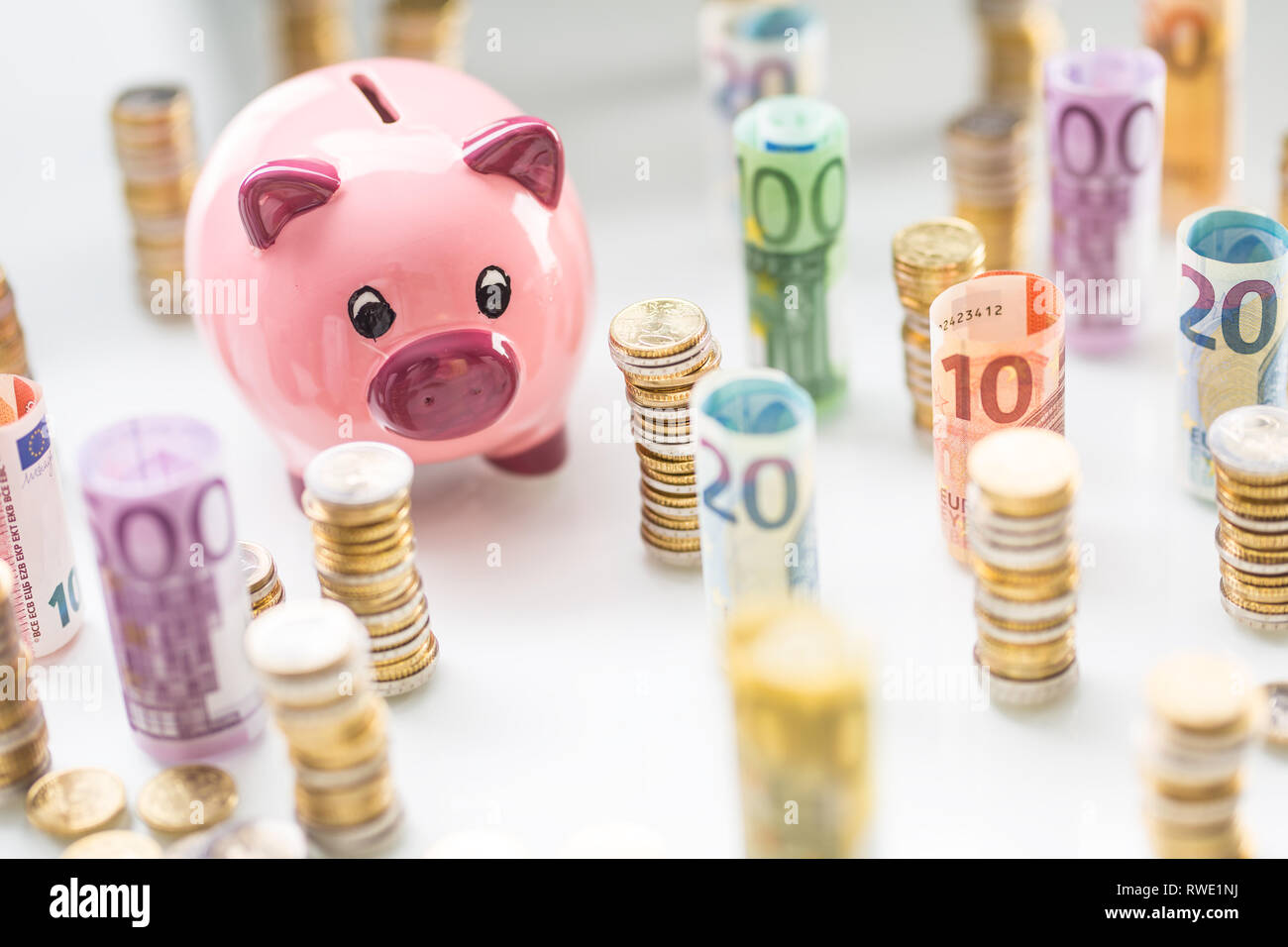 Rosa Sparschwein in der Mitte von gewalzten Euro-Banknoten und Türmen mit Münzen Stockfoto