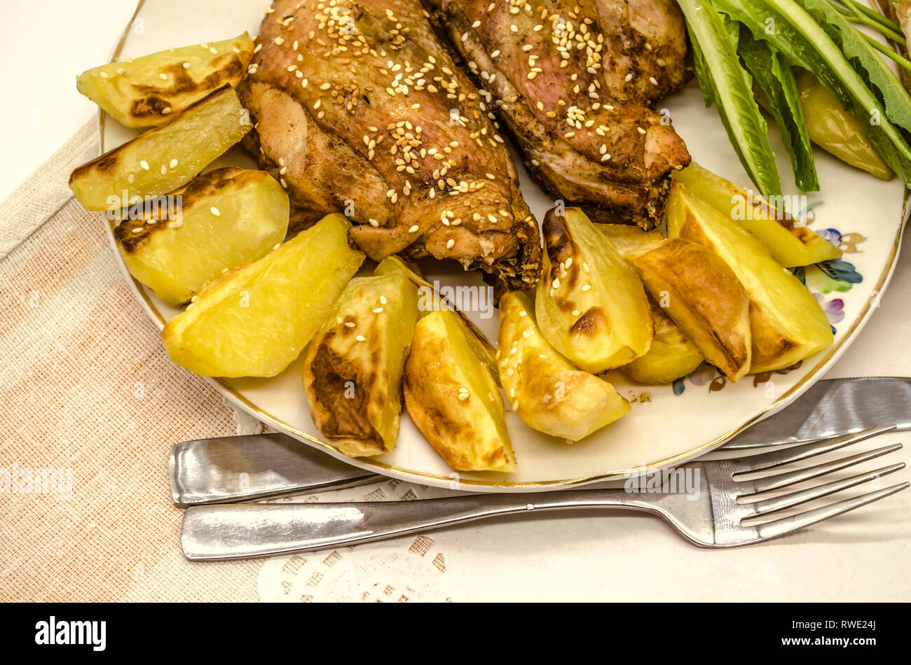 Fayence Platte mit Bratkartoffeln und Huhn, überzogen mit weißer Sesam und schwarzem Pfeffer, neben dem Salat Pfeffer liegen auf einem weissen Papier Serviette. Stockfoto