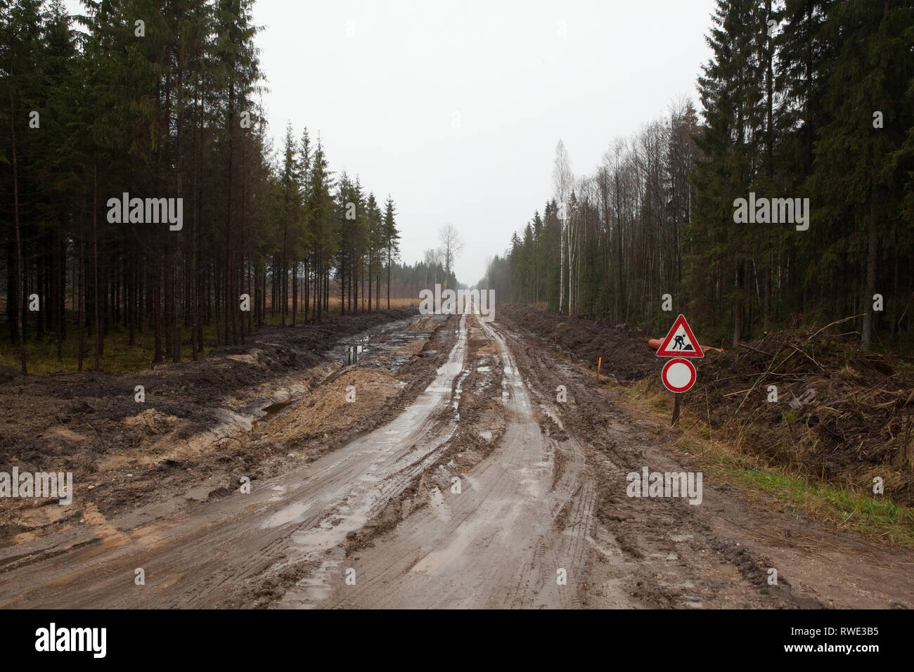 Schlammigen Feldweg mit Männern am Arbeitsplatz Zeichen durch den Wald läuft, Lettland Stockfoto