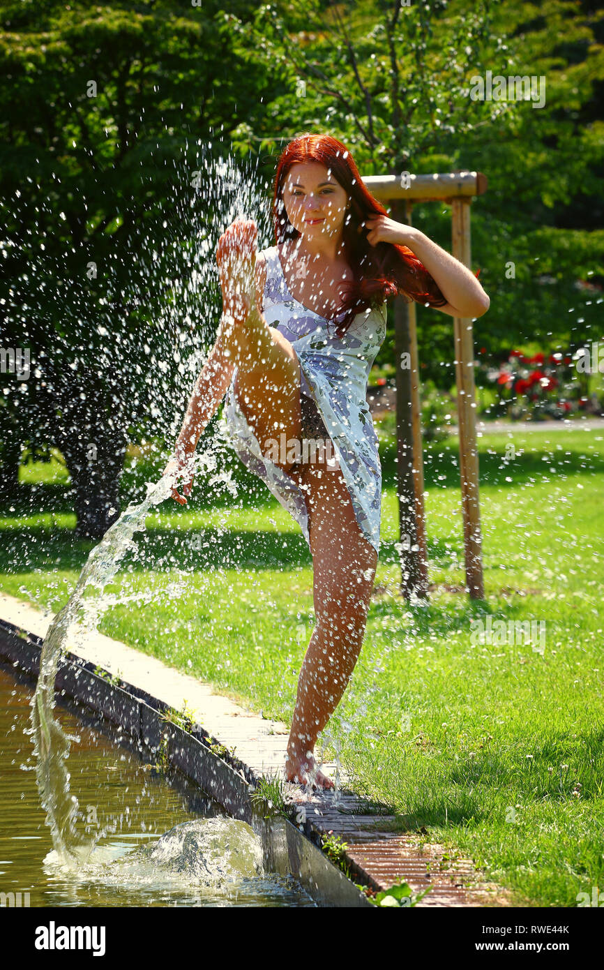 Eine junge Frau schafft ein Brunnen mit Ihrem Fuß an einem Teich in einem Park. Sie hat Spaß und genießt das schöne Wetter. Stockfoto