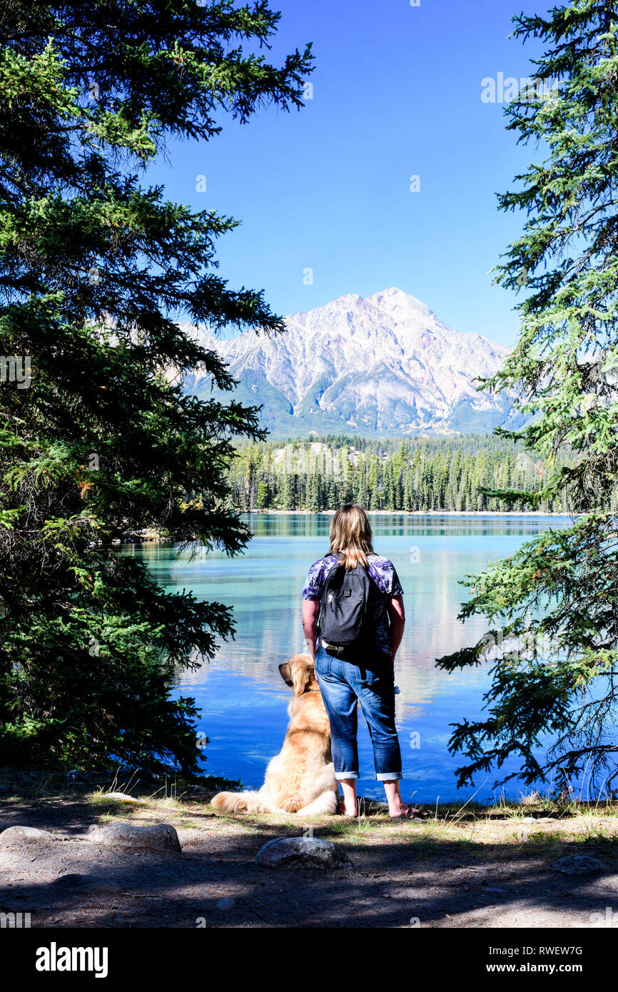 Eine Frau und ihr Golden Retriever machen eine Pause beim Wandern rund um den Lac Beauvert im Jasper National Park in Jasper, Alberta, Pyramid Mountain ist im Hintergrund Stockfoto