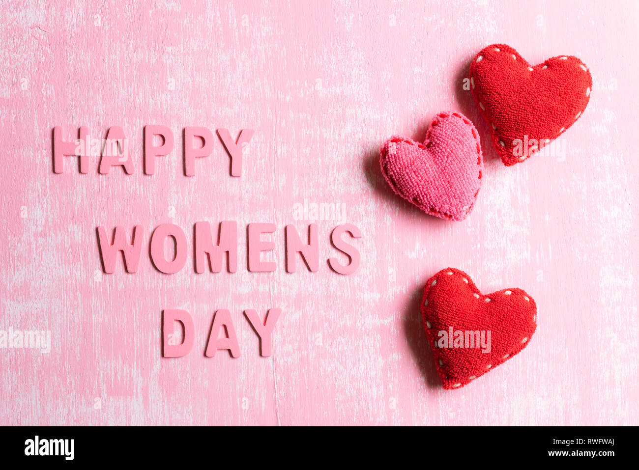 Tag der Frauen Konzept. Rote Herzen mit Holz Buchstaben bilden Wort Happy Tag der Frauen auf rosa und weißen Holzmöbeln Hintergrund geschrieben. Stockfoto