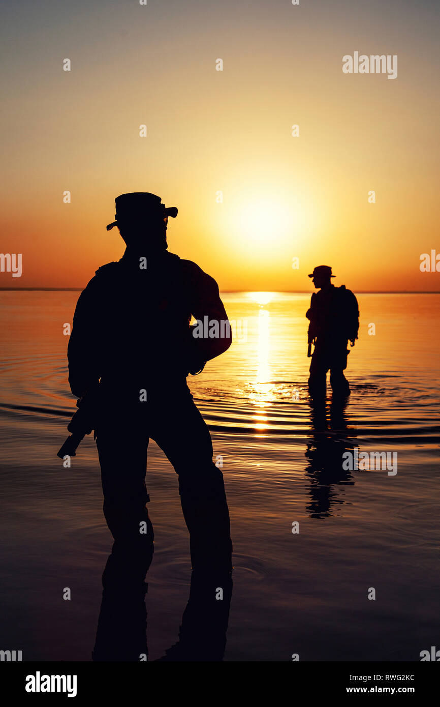Silhouette von Soldaten, die einen Fluß überquert, gegen eine orange Sonnenuntergang. Stockfoto
