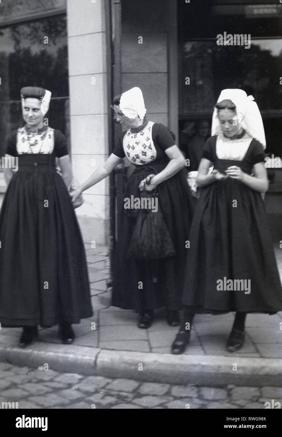 1950er Jahre, drei Frauen außerhalb stehend auf einem Bürgersteig, die traditionelle Kleidung der lange schwarze Röcke und weisse Haarnetze, Brüssel, Belgien. Stockfoto