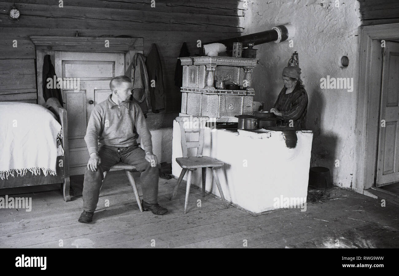 1930, in der Tschechoslowakei, dem Sudetenland, ein männlicher Landarbeiter in seiner ländlichen Wohn- und Schlafbereich, während seine Mutter im gleichen Raum eine Mahlzeit für ihn auf einer grundlegenden Herd bereitet. Stockfoto