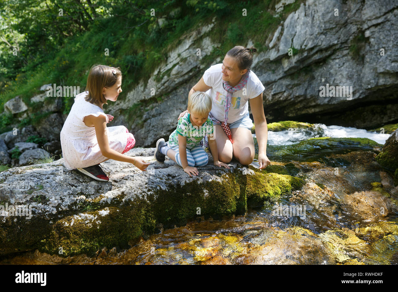 Mutter mit Kindern reden, Trinkwasser aus einer rein, frisch und kühl Mountain Stream auf einer Reise mit der Familie. Lebensstil im Freien, natürlichen Parenting, Kindheit Stockfoto