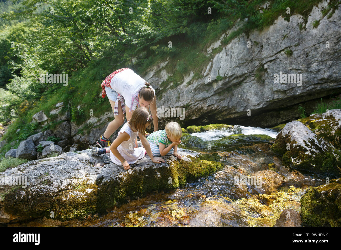 Mutter mit Kindern von Trinkwasser aus einer rein, frisch und kühl Mountain Stream auf einer Reise mit der Familie. Lebensstil im Freien, natürlichen Parenting, Kindheit erleben Stockfoto