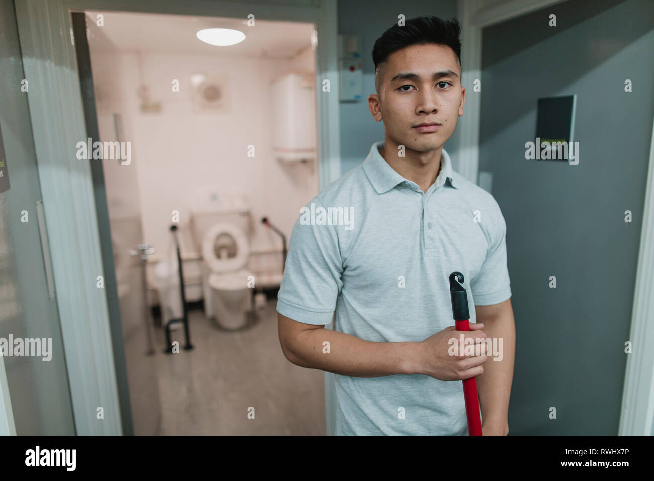 Portrait einer jungen, männlichen Reiniger bei der Arbeit. Er hält einen Mop. Stockfoto