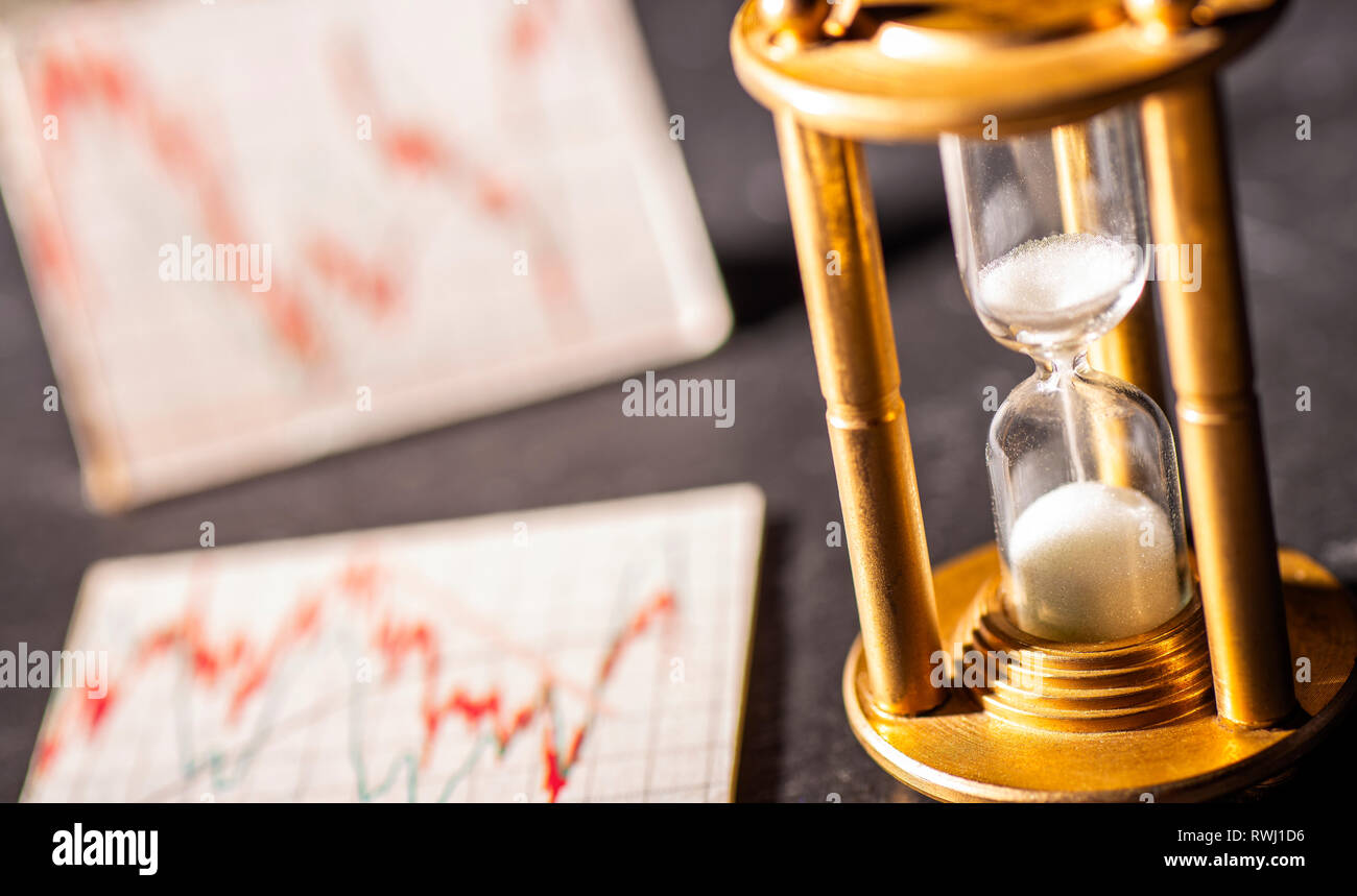 Sand rieselt durch eine Sanduhr mit Grafiken zeigen die Aktienkurse im Hintergrund. Symbol für den Faktor Zeit bei der Investition. Stockfoto