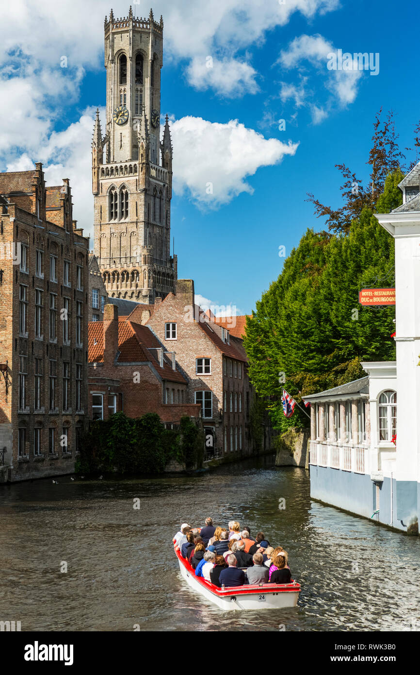 Kleine Tournee Boot mit Menschen in einem Kanal mit großen gotischen Kirchturm im Hintergrund; Brügge, Belgien. Stockfoto