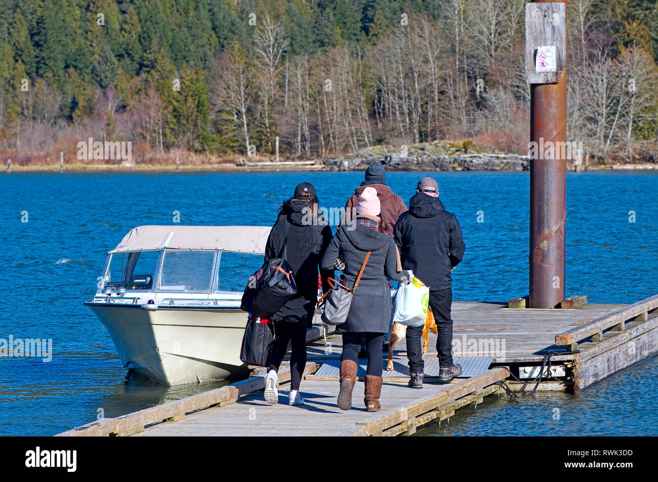 Vier junge Leute im Winter Kleider tragen über Nacht Taschen zu einem Verankerten Boot. Grant verengt Regional Park, Pitt Meadows, B.C. Kanada Stockfoto