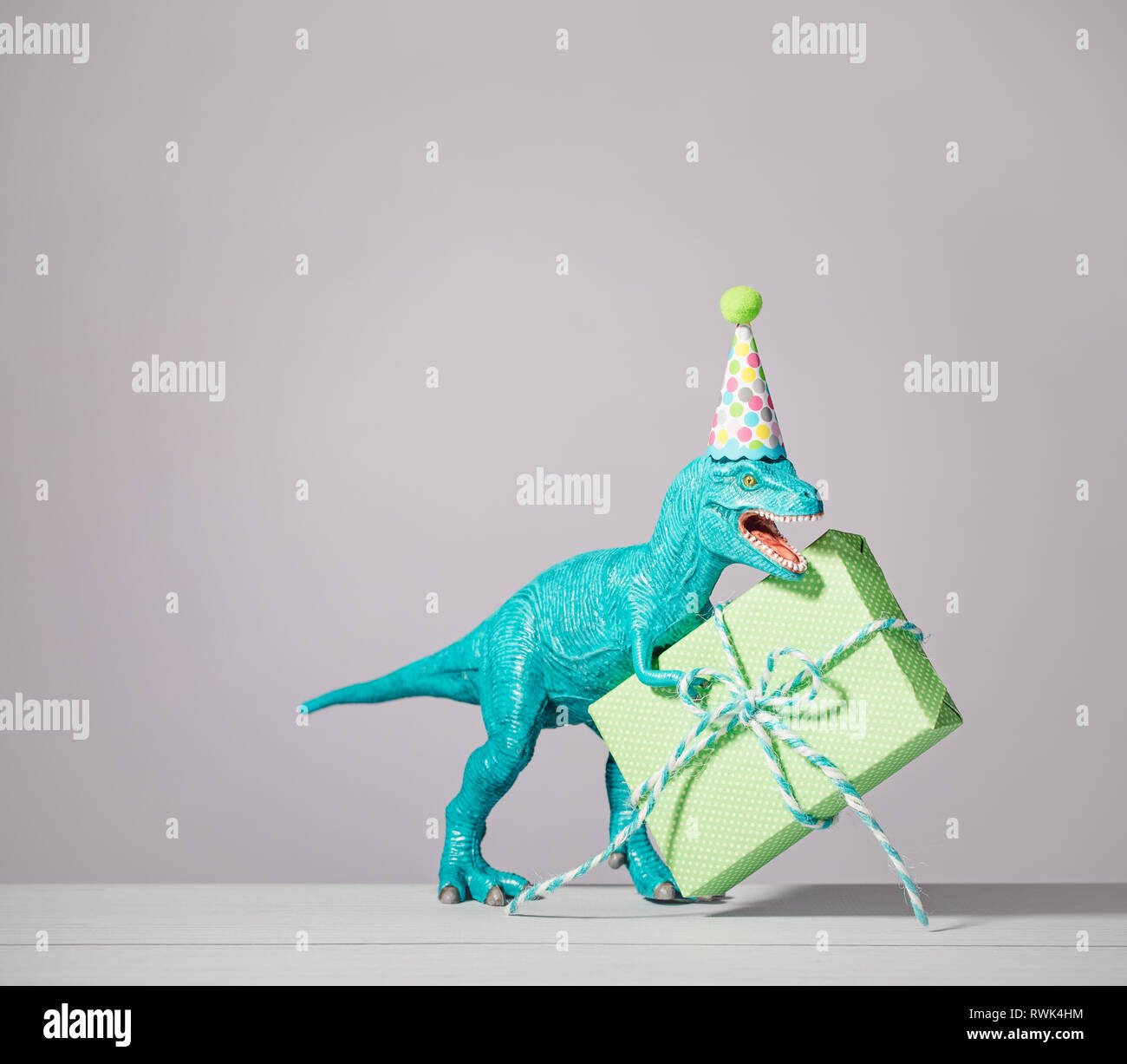 T-rex Dinosaurier Spielzeug mit geburtstagsmütze Holding Geschenk auf einen hellgrauen Hintergrund. Stockfoto