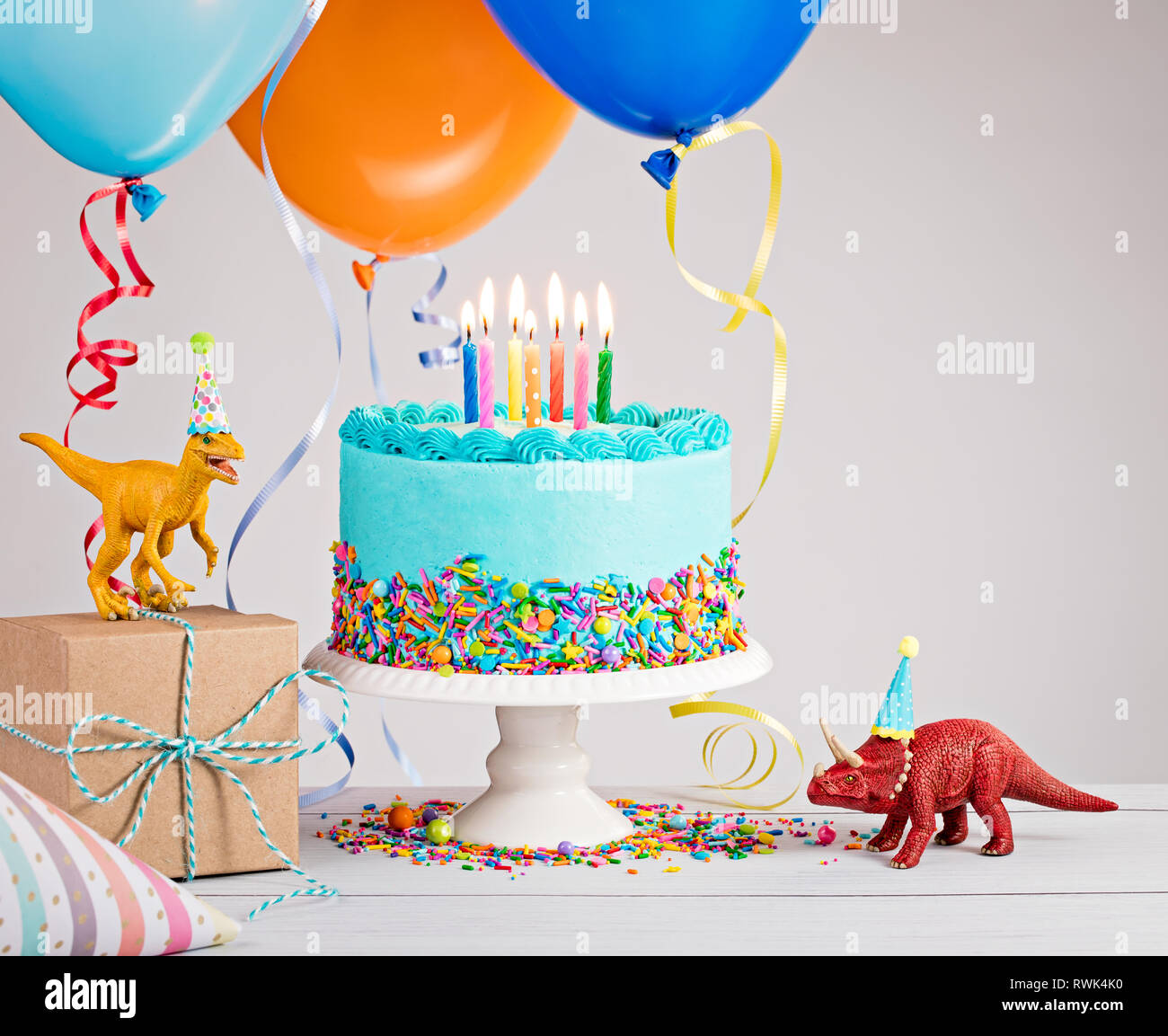 Childs Birthday Party Szene mit blauer Kuchen, Geschenkbox, Spielzeug Dinosaurier, Hüte und bunte Luftballons über Hellgrau. Stockfoto