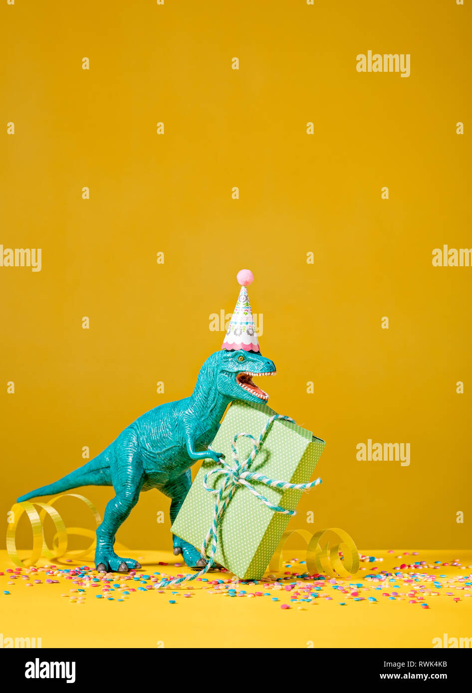 Spielzeug Dinosaurier mit Geburtstagsgeschenk das Tragen einer Partei hat auf einem gelben Hintergrund. Stockfoto