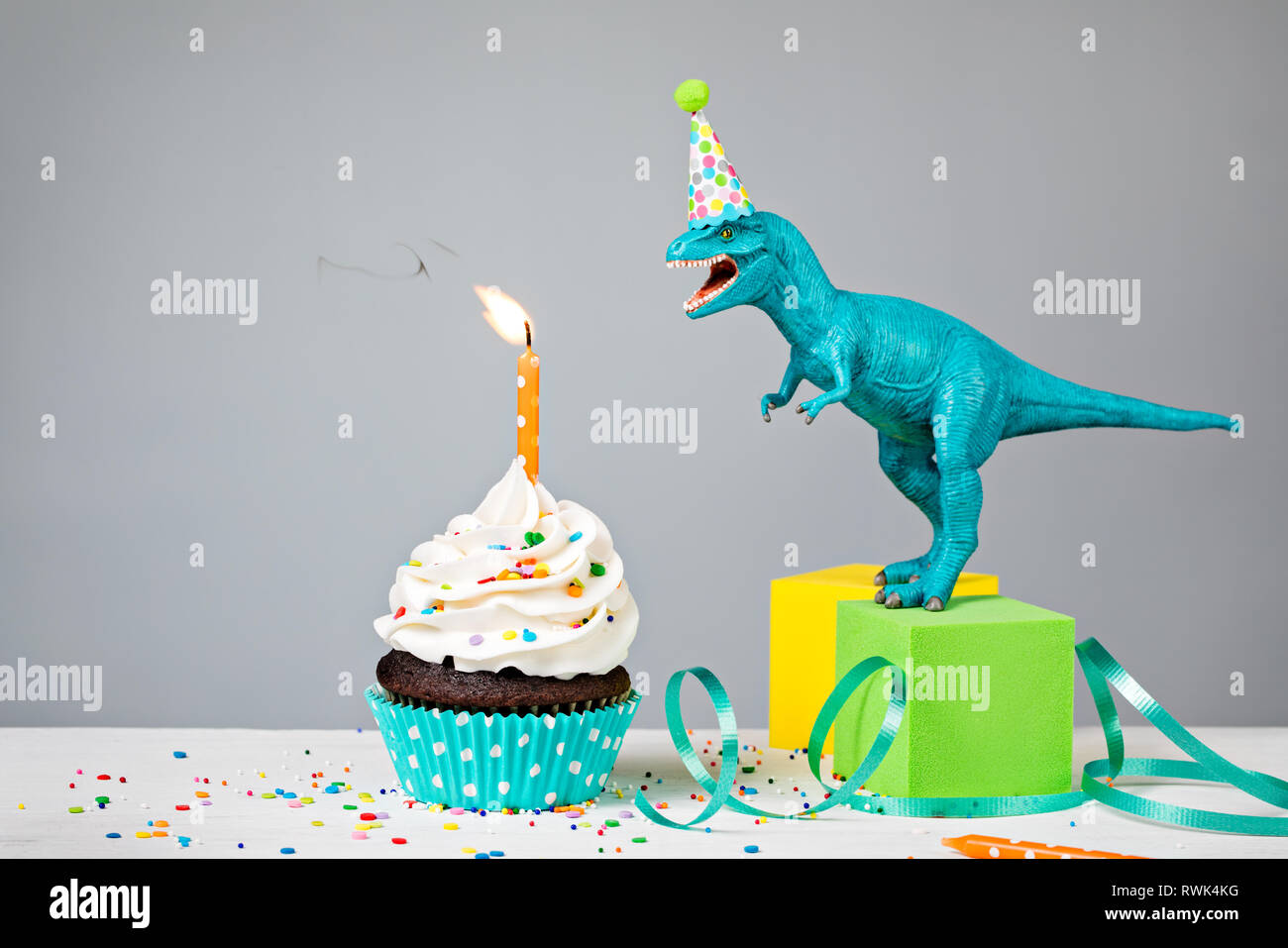 Spielzeug Dinosaurier Ausblasen Geburtstag Kerze mit Cup Cake auf grauem Hintergrund Stockfoto