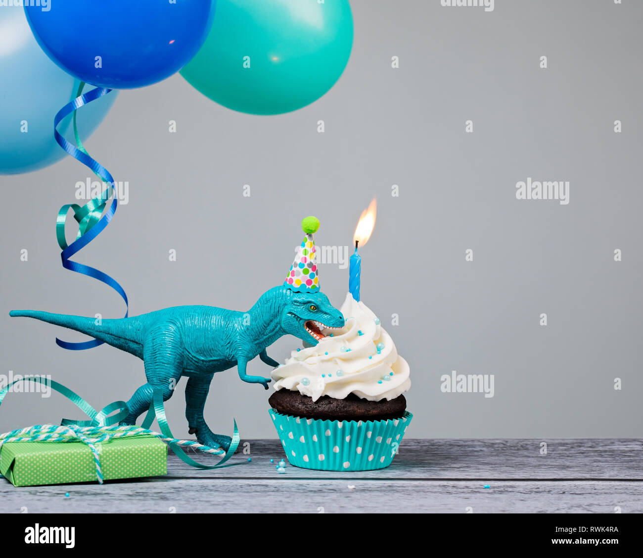 Blauer Dinosaurier Spielzeug essen Geburtstag Cupcake auf grauem Hintergrund. Stockfoto