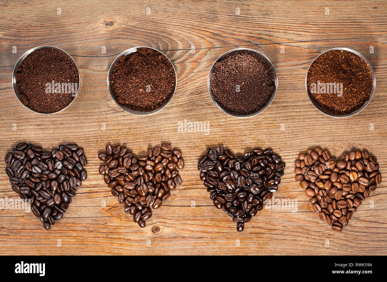 Ansicht von oben von vier Sorten von gerösteten Kaffeebohnen in der Form der Herzen mit ihren frisch gemahlenen Pendants in kleinen Schälchen auf braunem Holz- Stockfoto