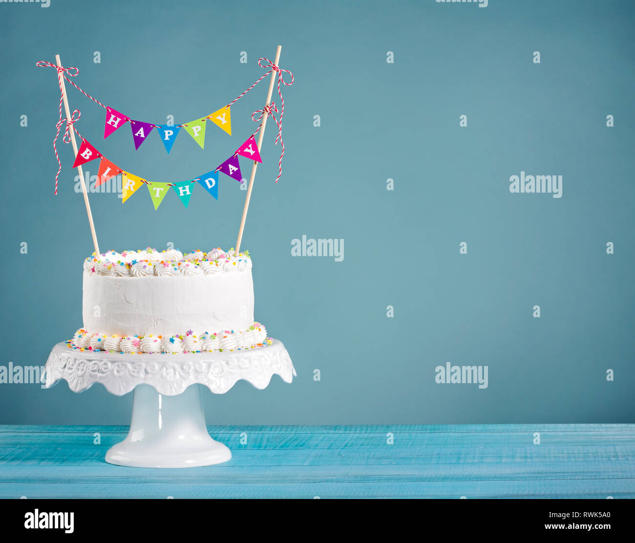 Weiß Buttercream Geburtstagskuchen mit bunten Bunting und Streuseln über blauer Hintergrund Stockfoto