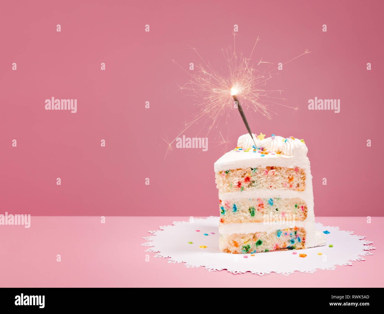 Scheibe der Bunten Geburtstag Konfetti Kuchen mit einer brennenden Wunderkerze über einen rosa Hintergrund. Stockfoto