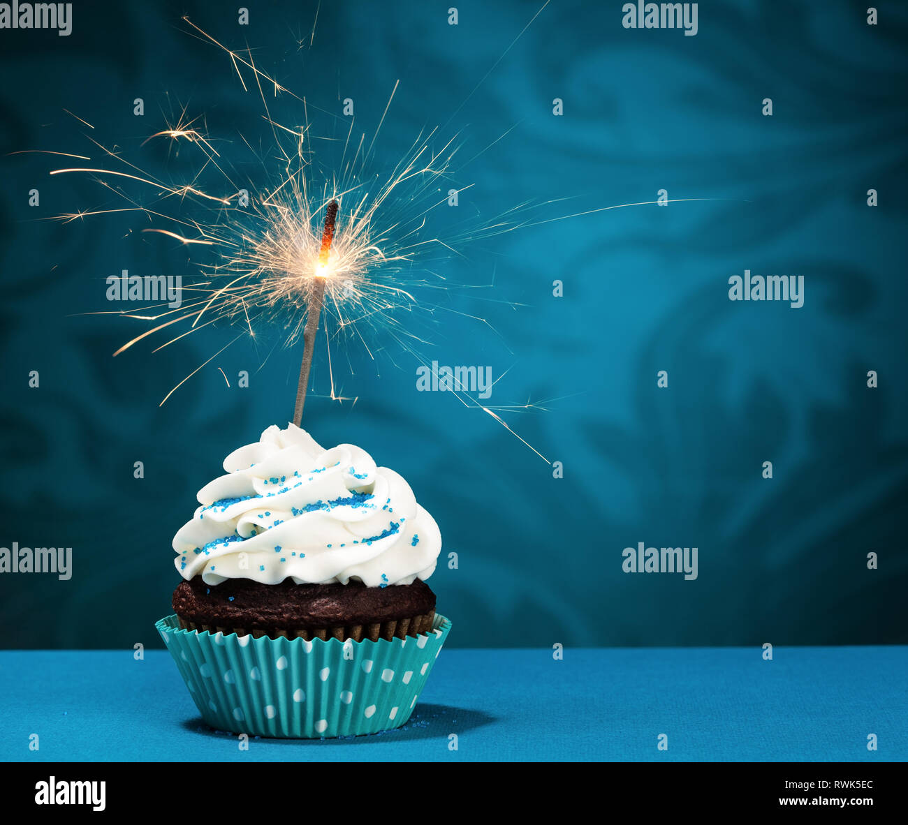 Cupcake mit Streuseln und eine Wunderkerze über einen blauen Hintergrund. Stockfoto