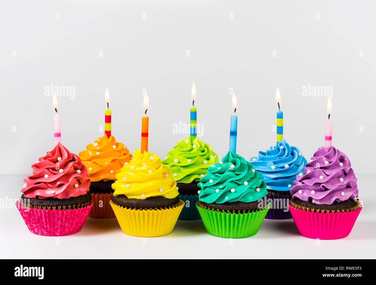 Reihen von bunten cup cakes mit Geburtstag Kerzen dekoriert und Streuseln. Stockfoto