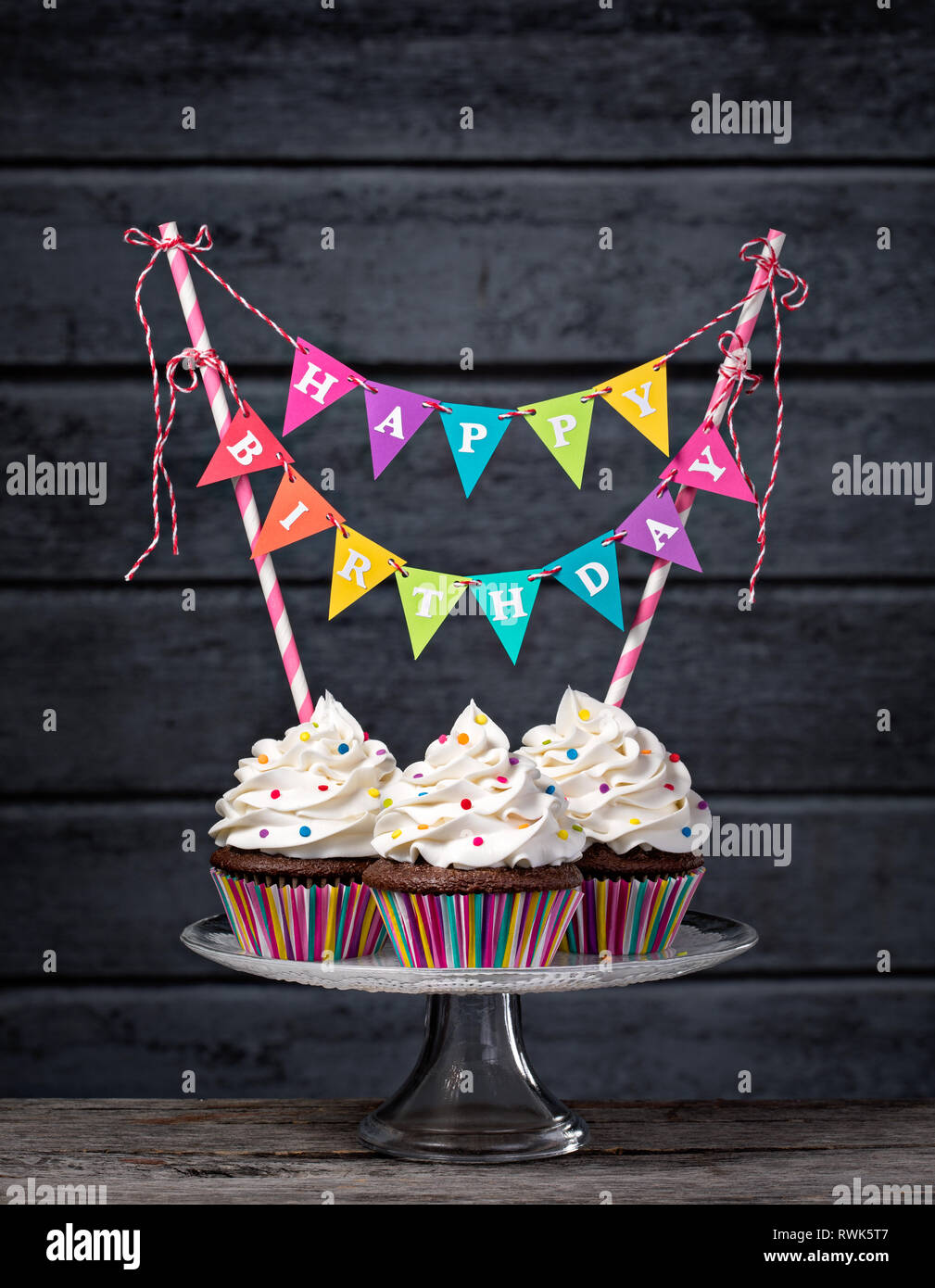 Drei schoko Cupcakes mit vanilla buttercream Vereisung, besprüht, und einen bunten Happy Birthday Banner. Stockfoto