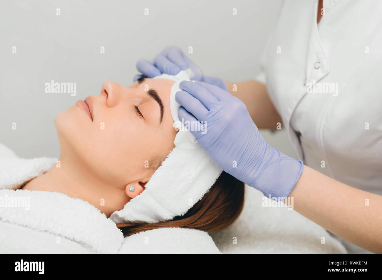 Kosmetikerin abwischen Gesicht zu Ihrem Patienten vor der Behandlung der Haut Stockfoto