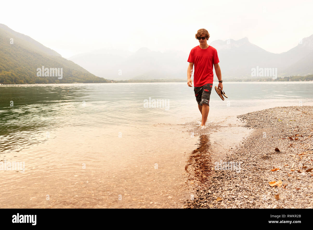 Junger Mann paddeln Knöchel tief in den See von Annecy, Annecy, Rhône-Alpes, Frankreich Stockfoto