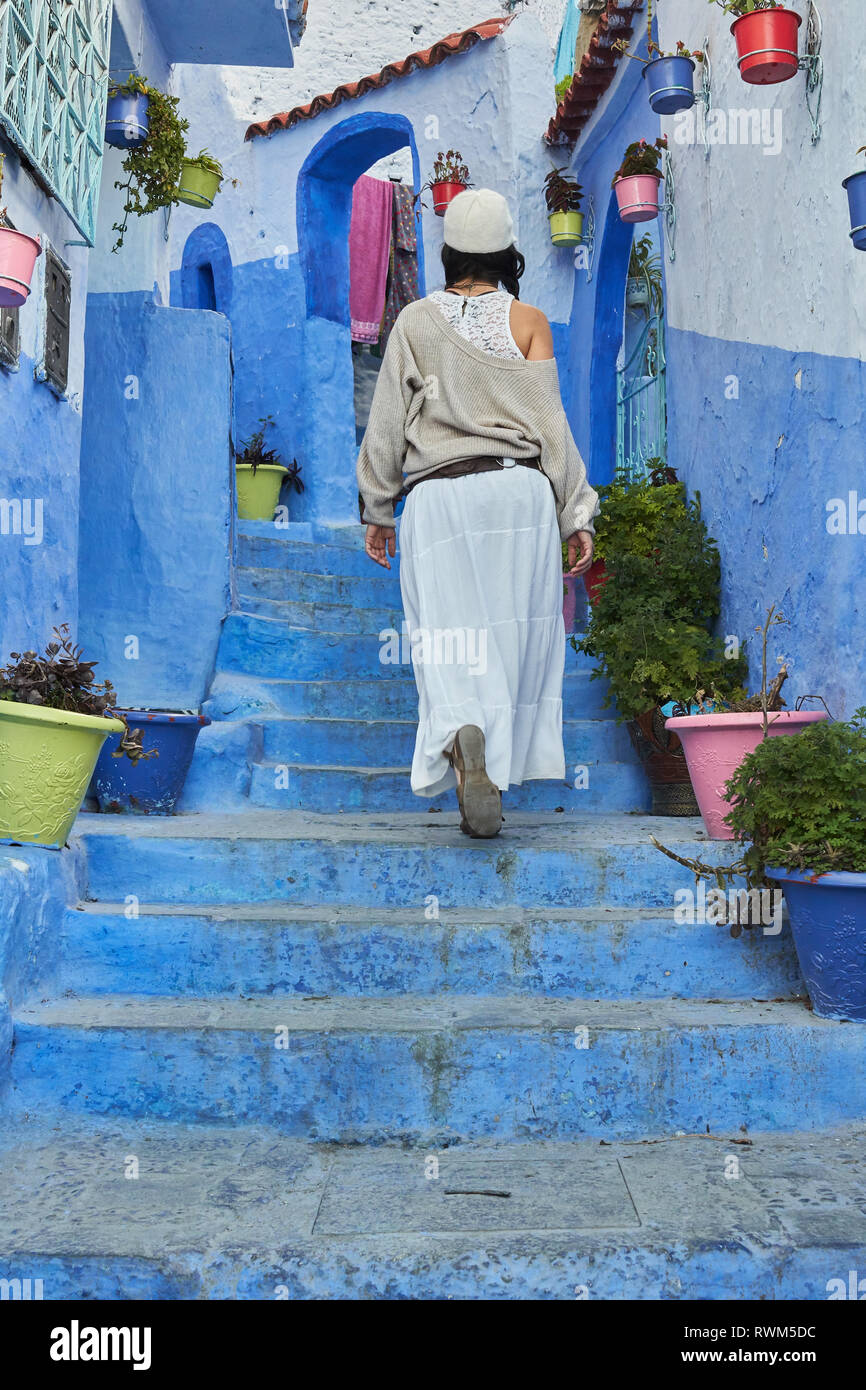 Rückansicht der Dame in Rock und Hut oben auf Blau Treppe in der Nähe von alten Häusern in Marrakesch, Marokko Stockfoto