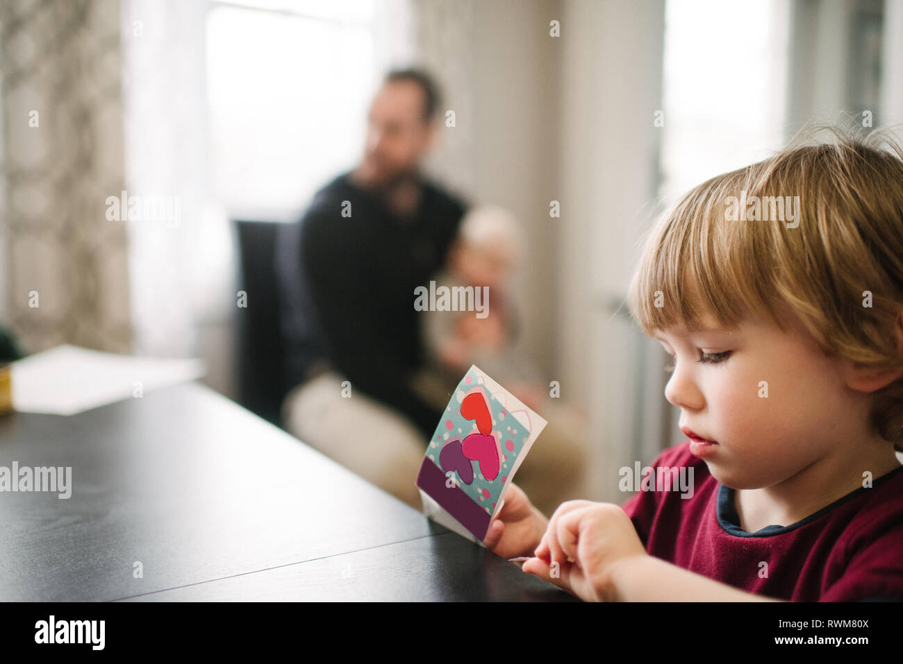 Junge spielt am Tisch, Vater im Hintergrund Stockfoto