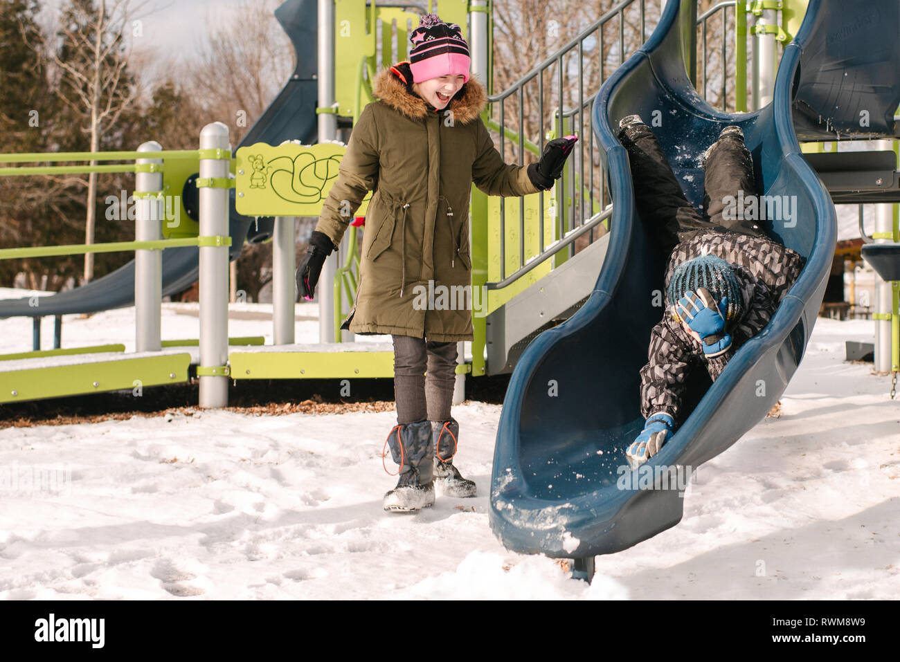 Mädchen beobachten Bruder kopfüber auf dem Spielplatz im Schnee schieben Stockfoto