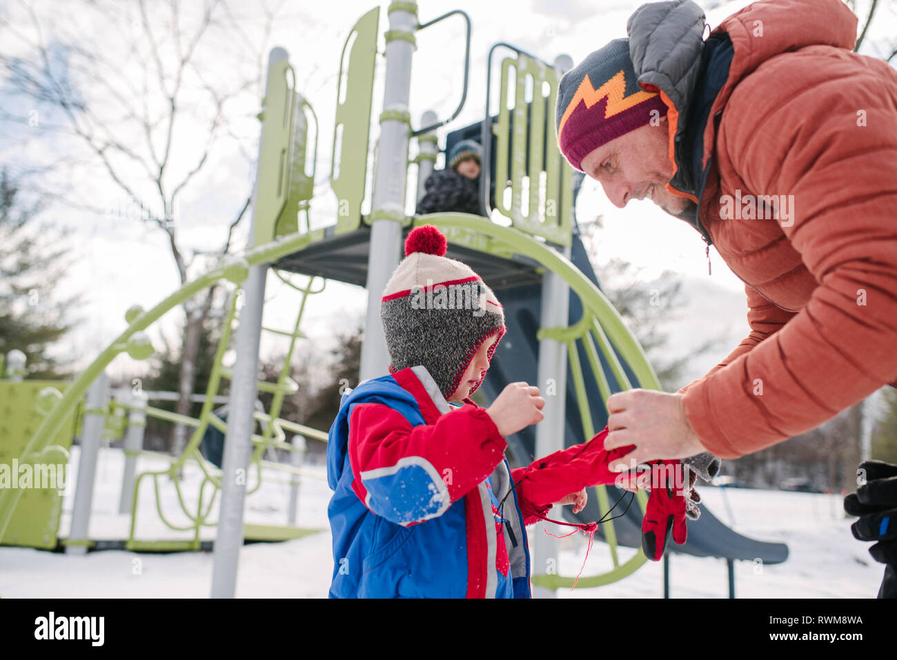 Vater setzen auf Handschuhe Boy's durch die rutschbahn im Schnee Stockfoto